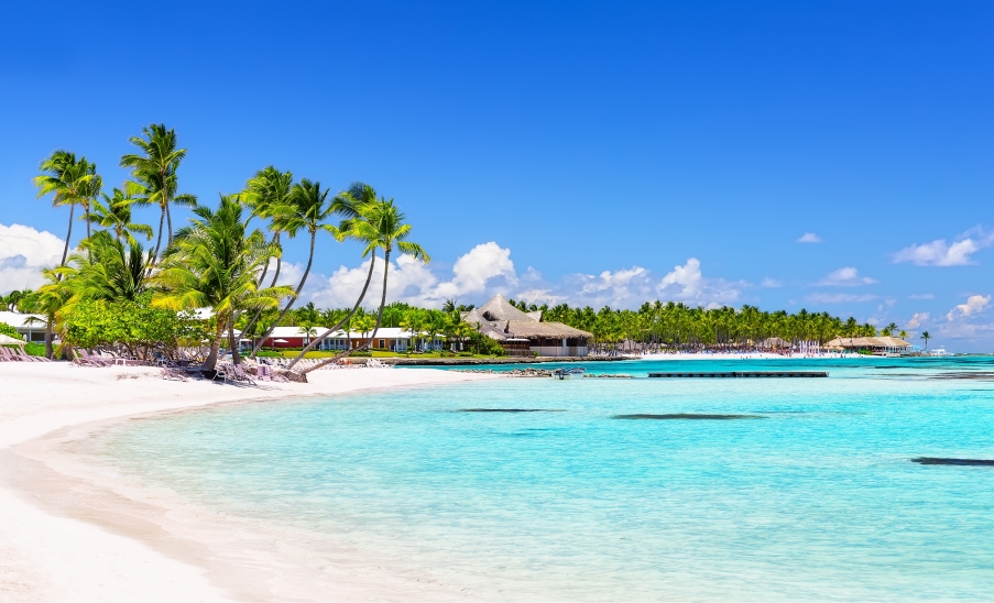 Punta Cana Praia de areia branca em Punta Cana com palmeiras, mar turquesa calmo e céu azul sem nuvens.