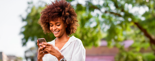 e-sim Mujer usando su teléfono móvil al aire libre, sonriendo, con árboles desenfocados de fondo.