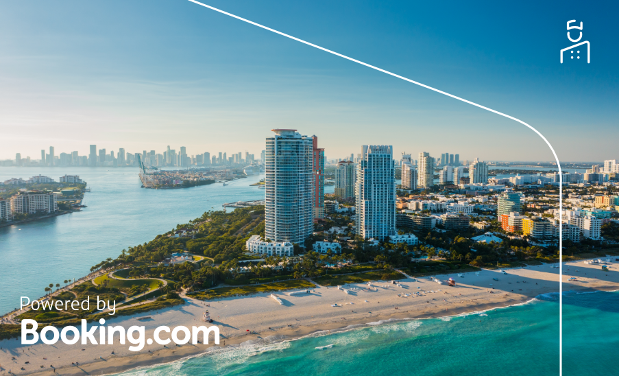 Vista aérea de South Beach em Miami, com prédios modernos à beira-mar e o oceano azul; “Powered by Booking.com”