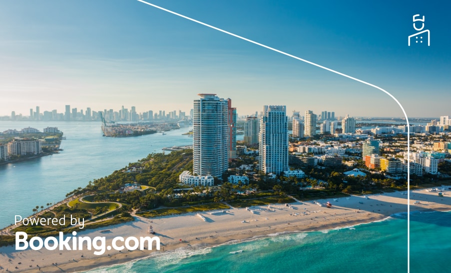Miami Vista aérea de South Beach em Miami, com prédios modernos à beira-mar e o oceano azul; “Powered by Booking.com”
