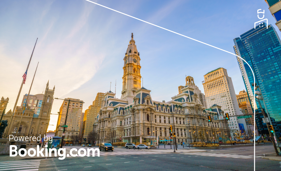 Vista do City Hall de Filadélfia ao pôr do sol, cercado por edifícios modernos; “Powered by Booking.com”