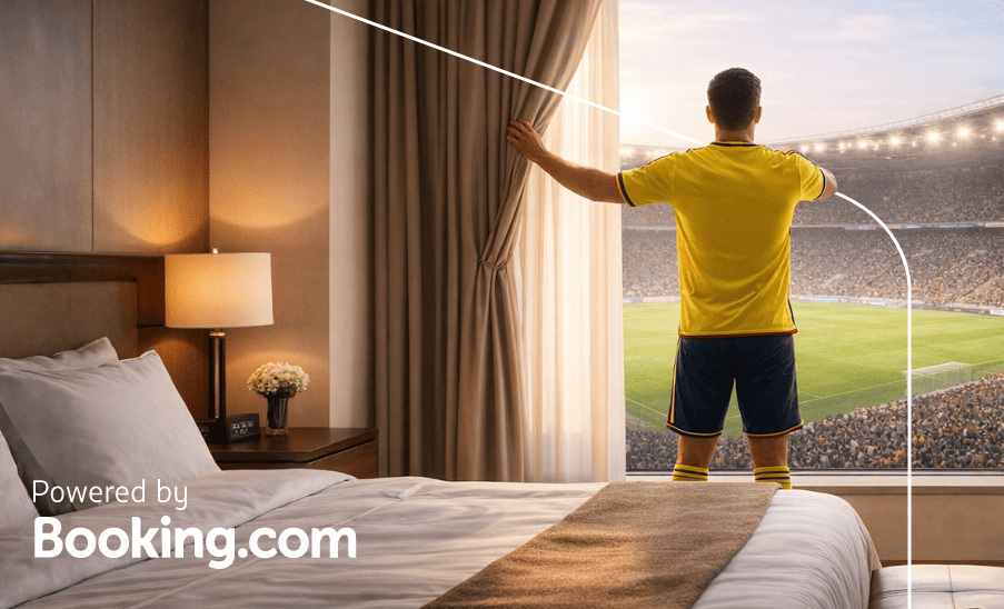 Hombre con camiseta amarilla de espaldas mirando el estadio desde la ventana de una habitación de hotel; “Powered by Booking.com
