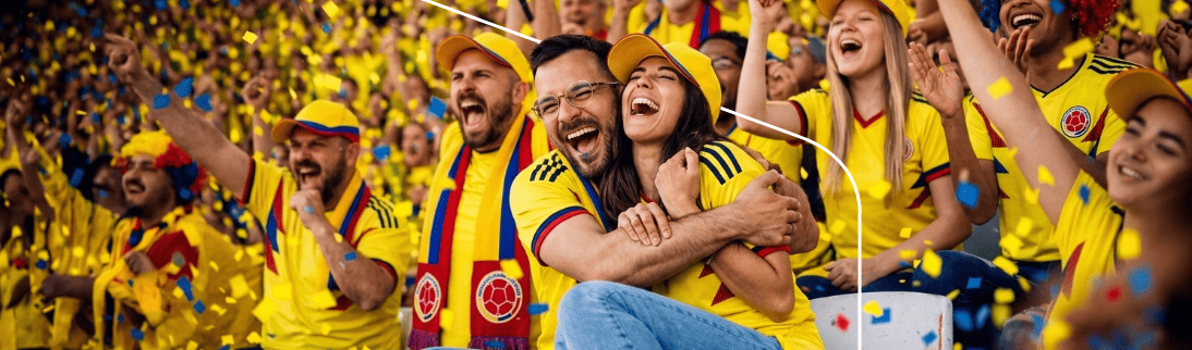 Pareja y multitud de aficionados colombianos celebrando entre confeti en las gradas de un estadio.