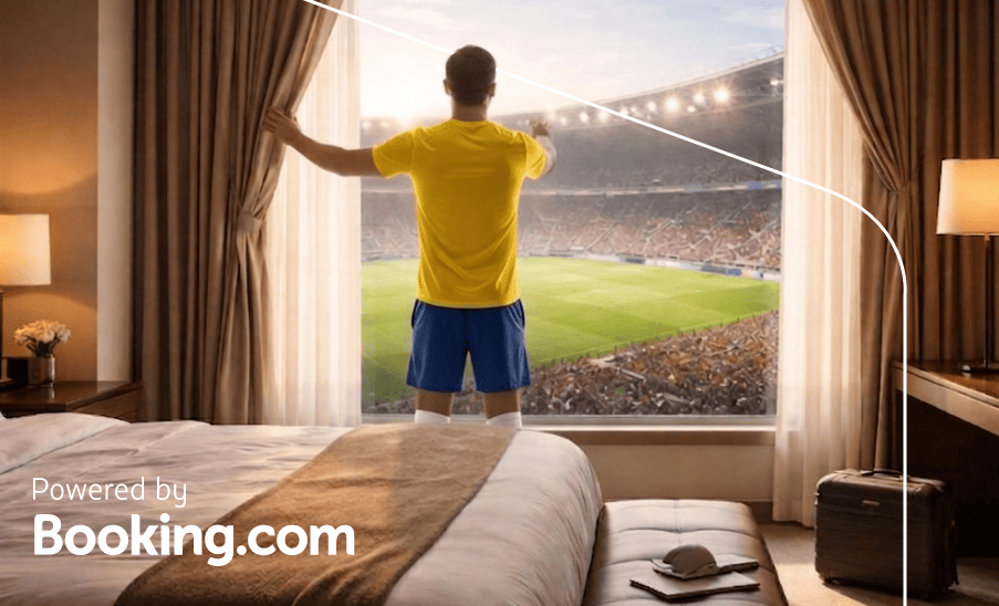 Nueva Jersey Hombre con camiseta amarilla de espaldas mirando el estadio desde la ventana de una habitación de hotel; “Powered by Booking.com