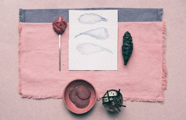 Kjolle Minimalist Peruvian plating on a pink and lavender table setting with tubers, a spoon, and watercolor sketches.